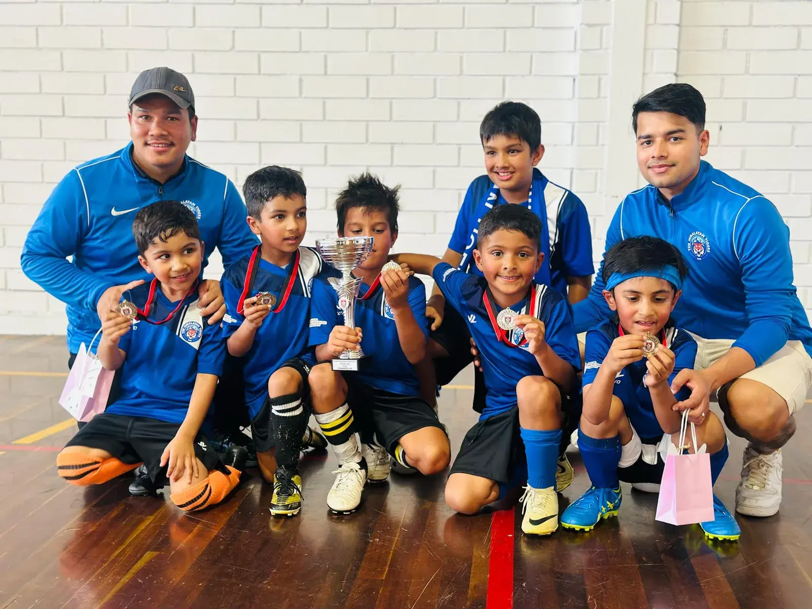 Young players and coaches with their trophies indoors