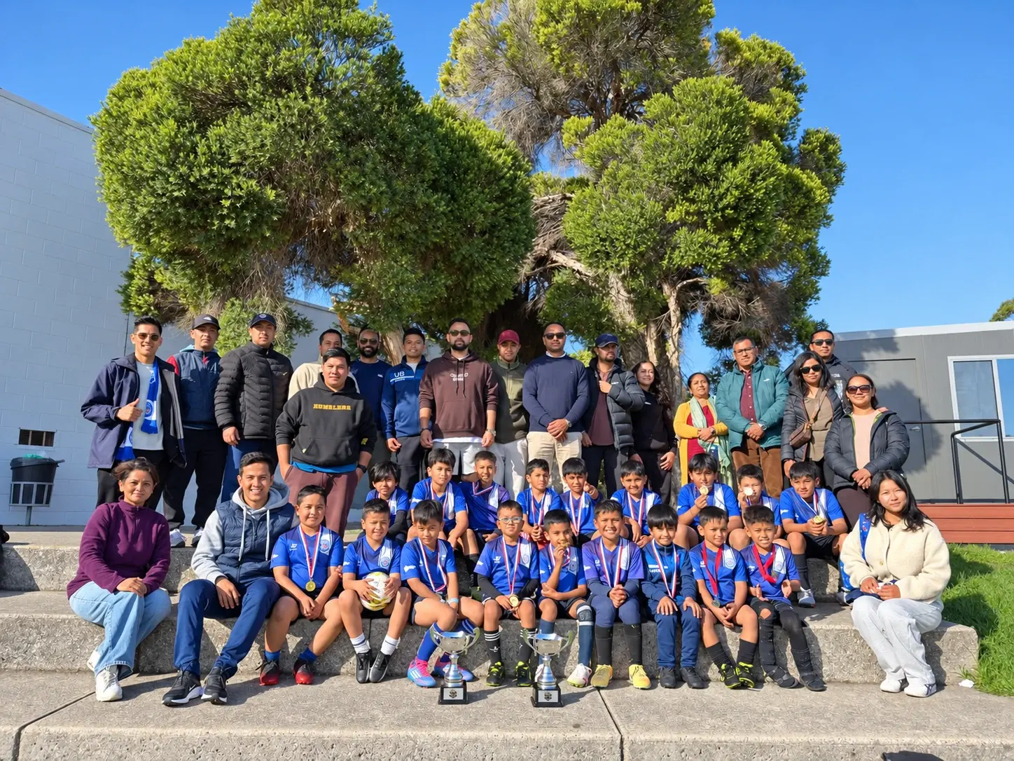 Young Tigers with their medals and trophies, surrounded by coaches and families